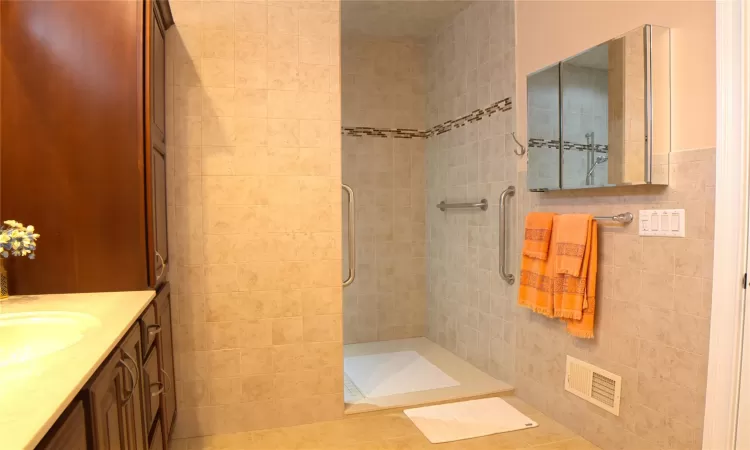 Bathroom featuring tile walls, visible vents, a tile shower, and vanity