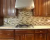 Kitchen with tasteful backsplash, stainless steel gas stovetop, ventilation hood, and light stone countertops