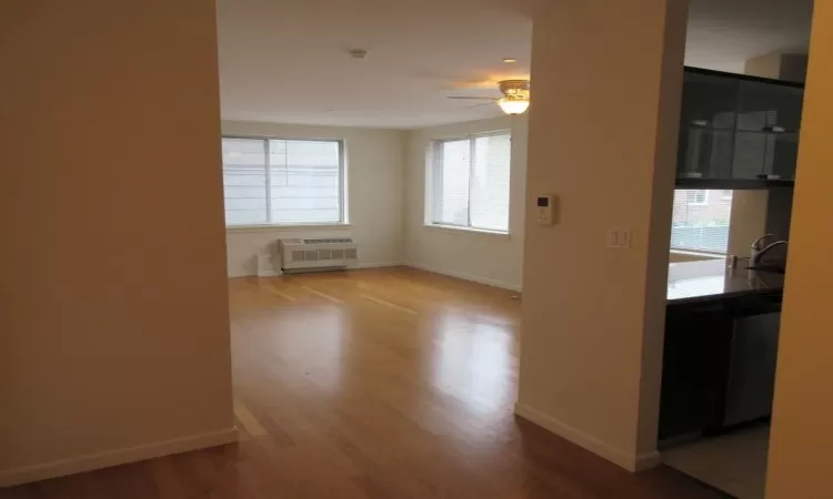 Empty room featuring baseboards, a ceiling fan, radiator, wood finished floors, and a sink