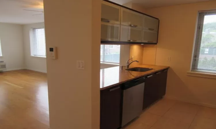 Kitchen with light stone counters, a sink, baseboards, dishwasher, and glass insert cabinets