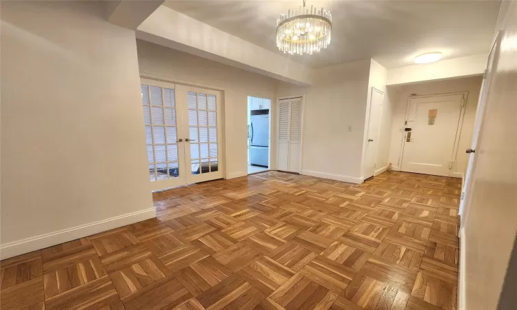 Spare room featuring a chandelier, french doors, and baseboards