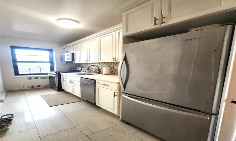 Kitchen featuring tasteful backsplash, radiator, stainless steel appliances, white cabinetry, and a sink