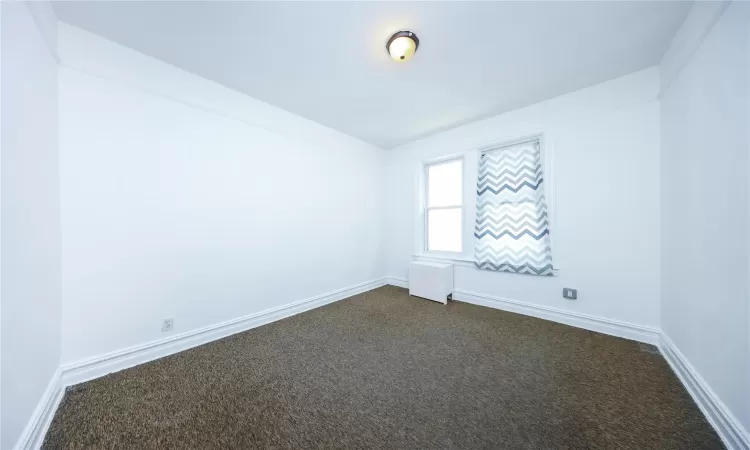 Unfurnished room with dark colored carpet, radiator, and baseboards