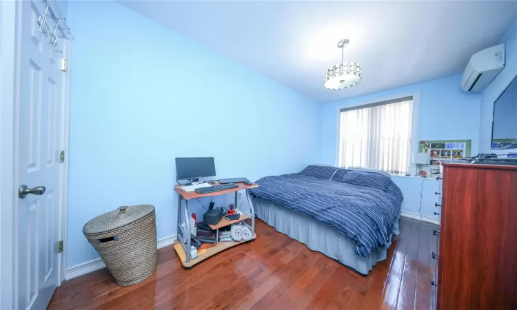 Bedroom featuring a wall mounted AC, hardwood / wood-style flooring, and baseboards