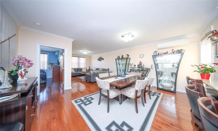 Dining space featuring light wood-style floors, a wall mounted air conditioner, crown molding, and baseboards