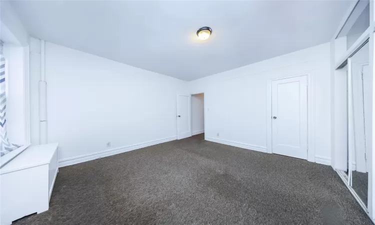 Unfurnished bedroom featuring radiator and dark carpet