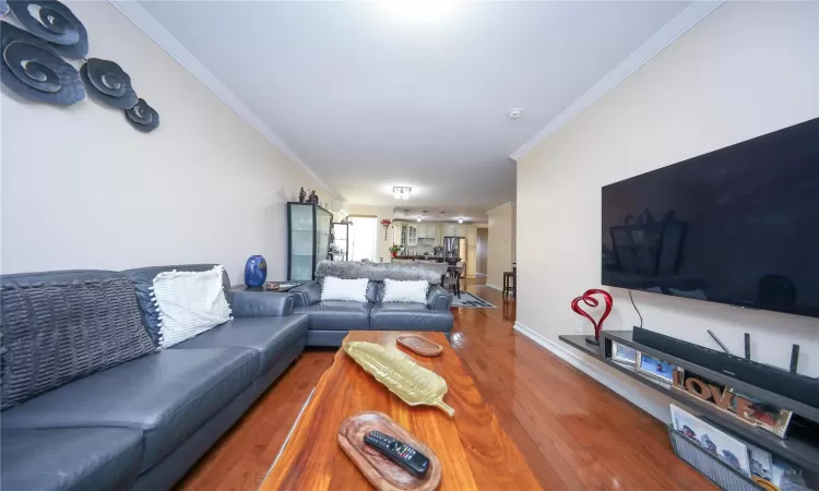 Living area with ornamental molding, wood finished floors, and baseboards