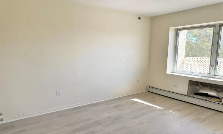 Unfurnished room featuring light wood-type flooring, a baseboard radiator, and baseboards