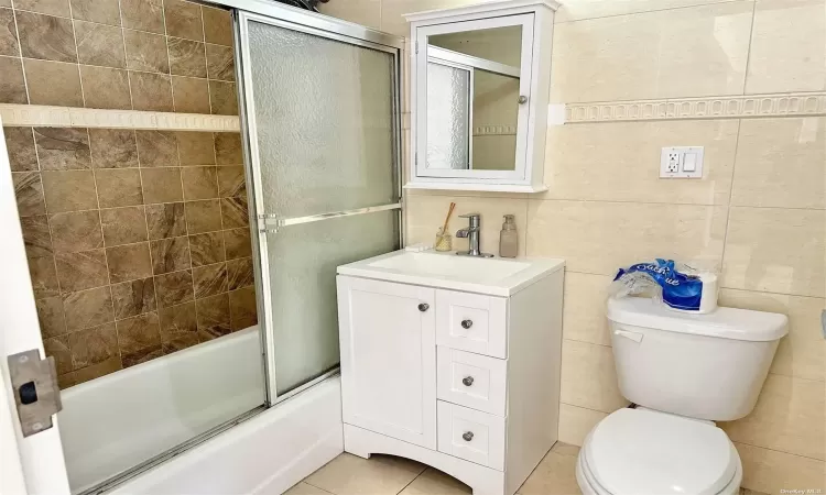 Full bathroom featuring tile patterned flooring, tile walls, toilet, and bath / shower combo with glass door