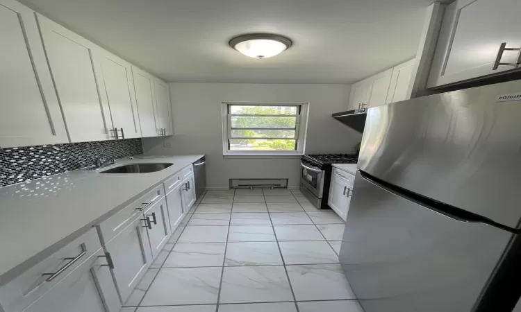 Kitchen featuring appliances with stainless steel finishes, a sink, marble finish floor, light countertops, and backsplash