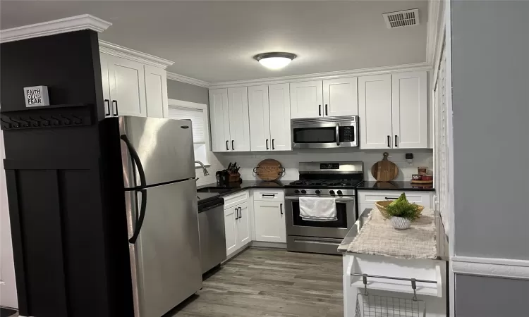 Kitchen with stainless steel appliances, visible vents, a sink, and white cabinetry