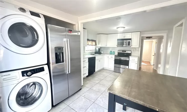 Kitchen featuring stacked washer and clothes dryer, light tile patterned floors, stainless steel appliances, light countertops, and white cabinetry