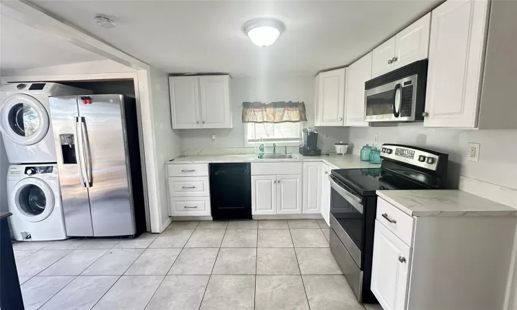 Kitchen featuring appliances with stainless steel finishes, stacked washer / drying machine, white cabinetry, a sink, and light tile patterned flooring