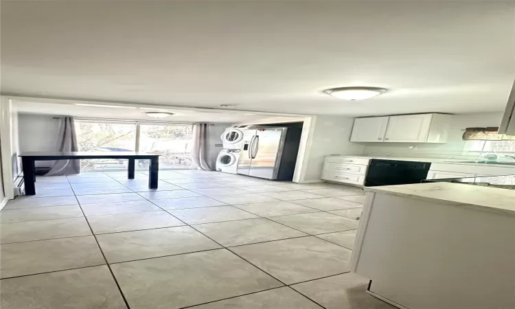 Kitchen featuring black dishwasher, stainless steel fridge, stacked washer / dryer, light stone counters, and white cabinetry