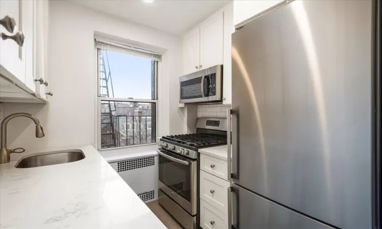 Kitchen featuring radiator, white cabinets, stainless steel appliances, and a sink