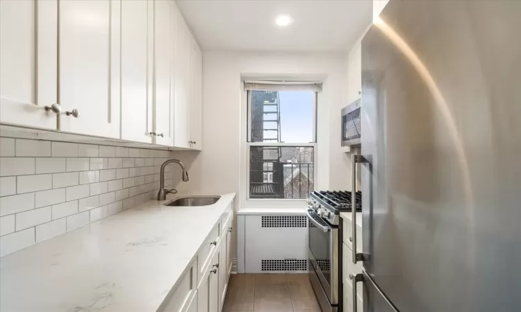 Kitchen featuring light stone counters, stainless steel appliances, tasteful backsplash, white cabinetry, and a sink