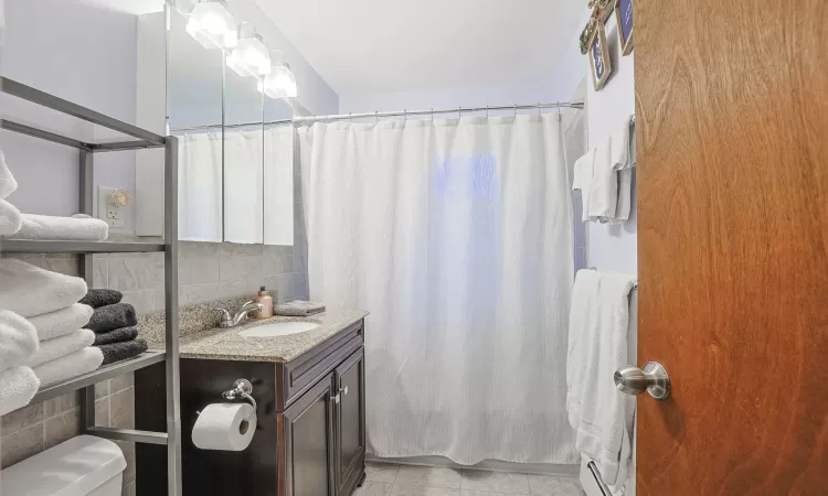 Full bathroom featuring curtained shower, backsplash, toilet, vanity, and tile patterned floors