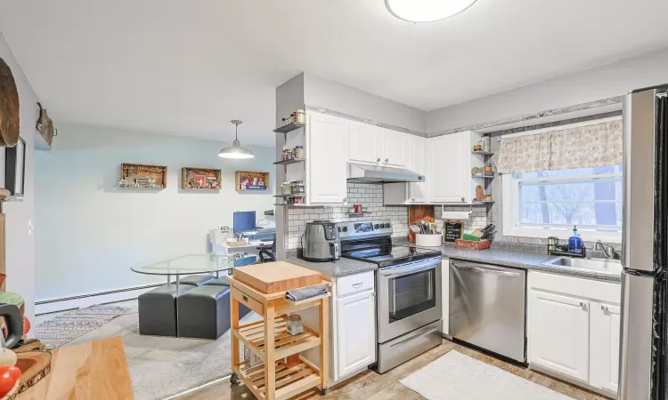 Kitchen with stainless steel appliances, under cabinet range hood, white cabinetry, open shelves, and a sink