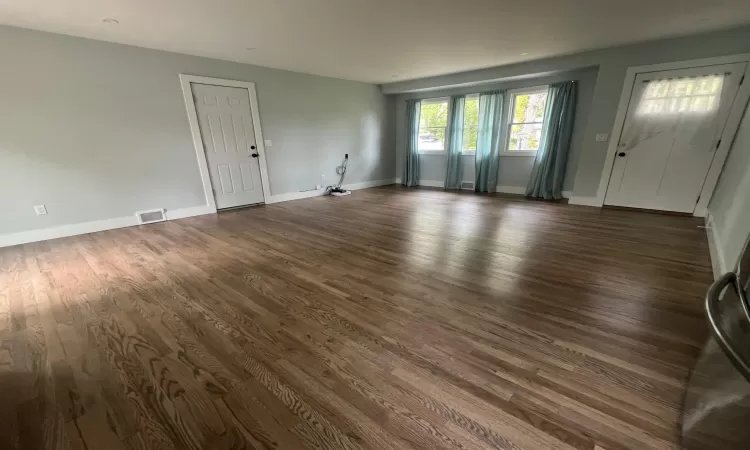 Empty room featuring visible vents, dark wood finished floors, and baseboards