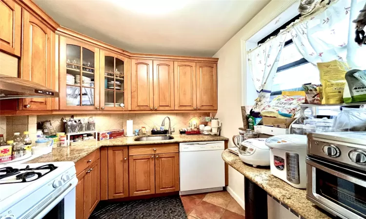 Kitchen featuring light stone counters, white appliances, a sink, backsplash, and glass insert cabinets