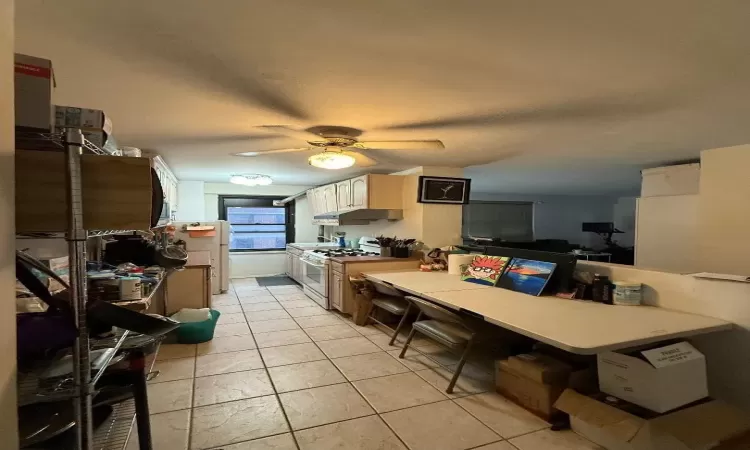 Kitchen with light tile patterned floors, under cabinet range hood, a ceiling fan, light countertops, and white gas range