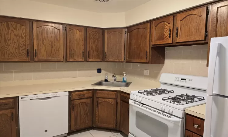 Kitchen with tasteful backsplash, light countertops, light tile patterned flooring, a sink, and white appliances