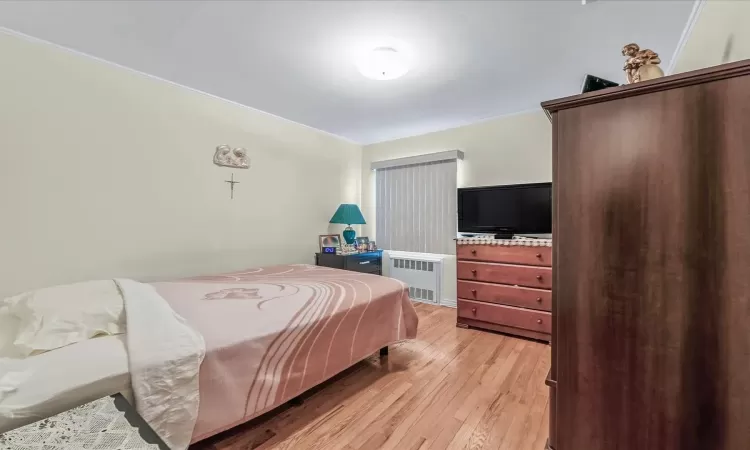 Bedroom with radiator, light wood-type flooring, and crown molding