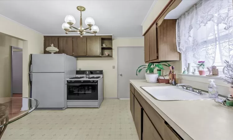 Kitchen featuring freestanding refrigerator, an inviting chandelier, white gas range, light countertops, and a sink