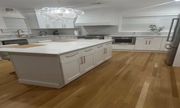 Kitchen with stainless steel appliances, visible vents, white cabinetry, a sink, and wall chimney range hood