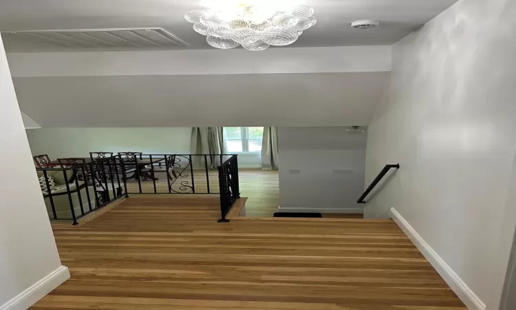 Stairway with a notable chandelier, wood finished floors, visible vents, and baseboards