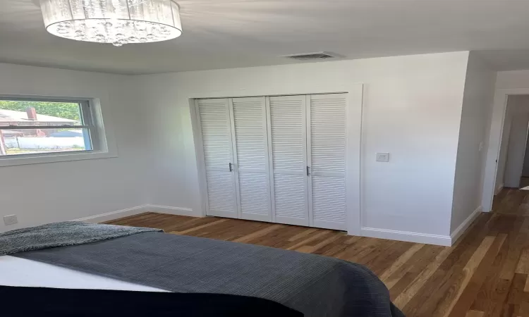 Unfurnished bedroom with a closet, wood finished floors, visible vents, and baseboards