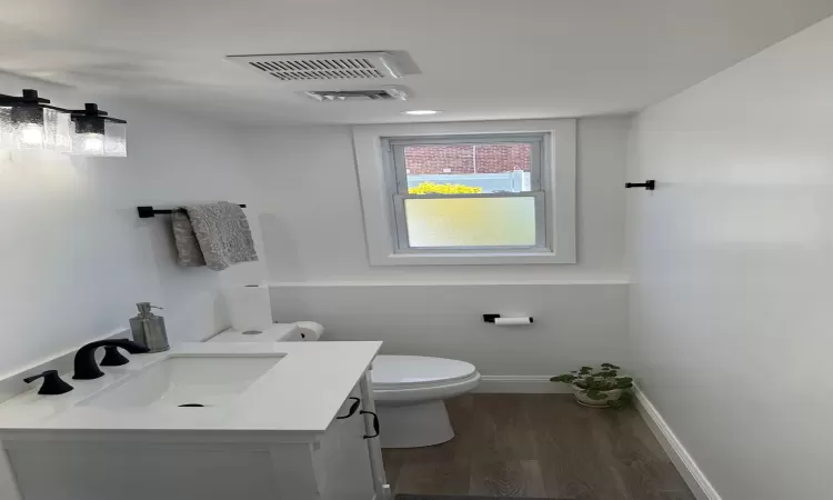 Bathroom with toilet, wood finished floors, vanity, visible vents, and baseboards