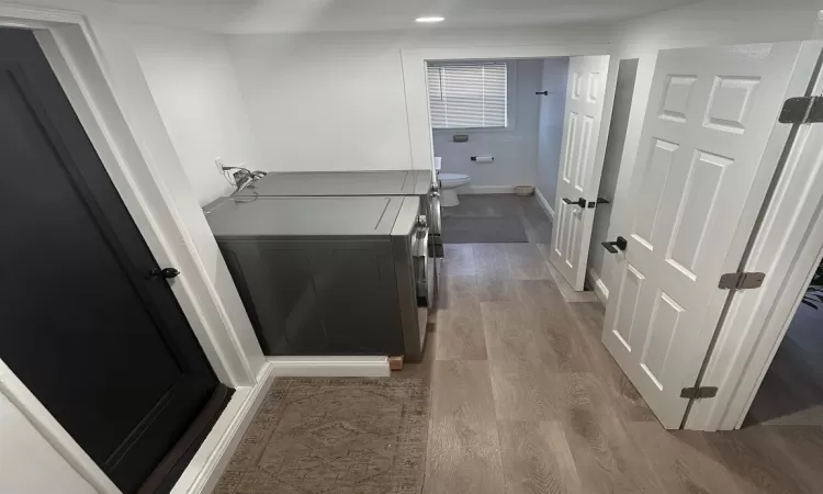 Bathroom with toilet, washing machine and dryer, baseboards, and wood finished floors