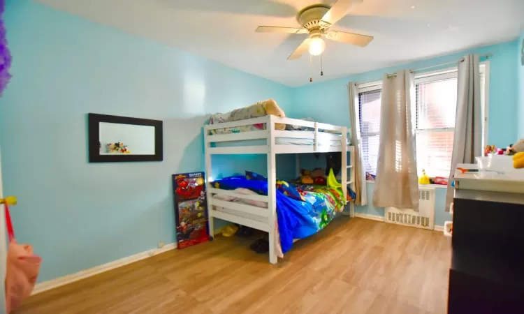 Bedroom with baseboards, ceiling fan, radiator heating unit, and wood finished floors