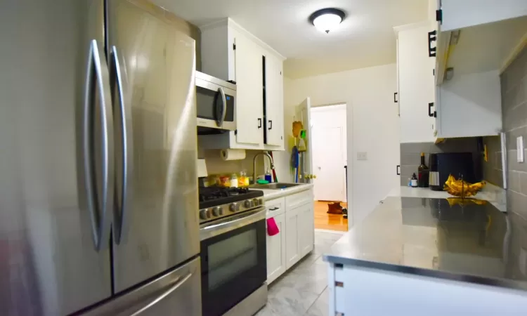 Kitchen with tasteful backsplash, appliances with stainless steel finishes, light countertops, white cabinetry, and a sink