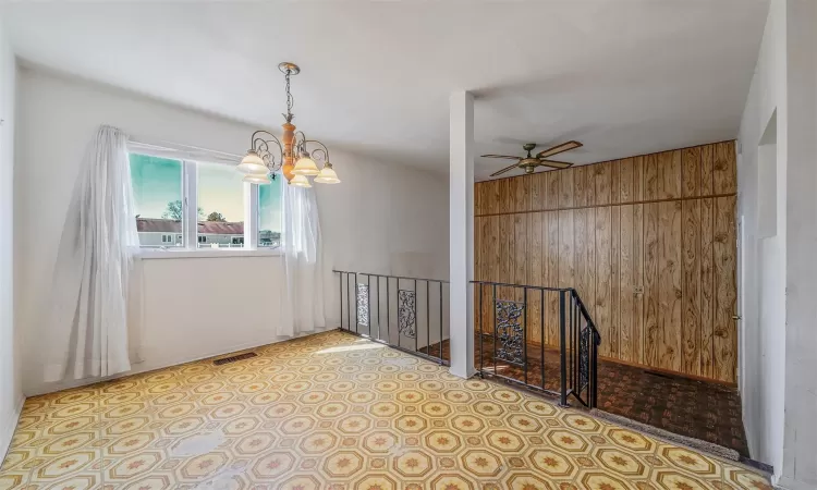 Spare room featuring wood walls, visible vents, and ceiling fan with notable chandelier