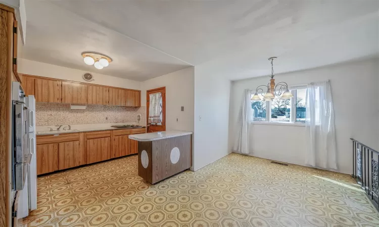 Kitchen featuring a chandelier, light countertops, hanging light fixtures, backsplash, and brown cabinetry