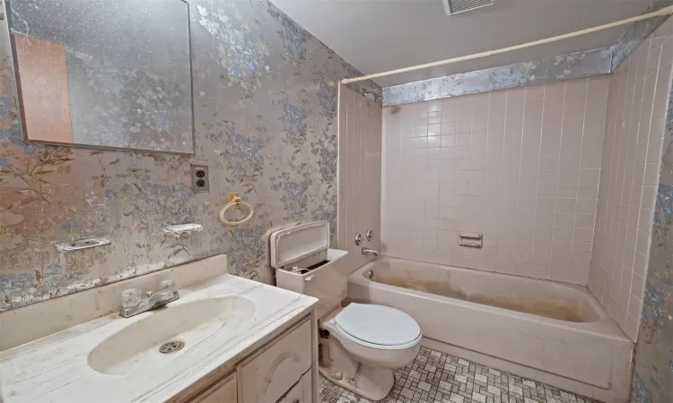 Bathroom with shower / washtub combination, vanity, toilet, and wallpapered walls