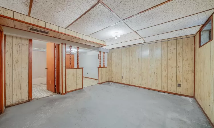 Finished below grade area with wood walls, baseboards, visible vents, and a drop ceiling