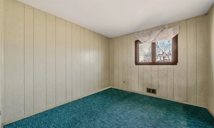 Spare room featuring carpet floors, visible vents, and wood walls