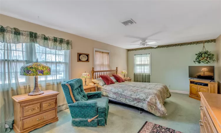 Bedroom with visible vents, a baseboard heating unit, a ceiling fan, light carpet, and baseboards