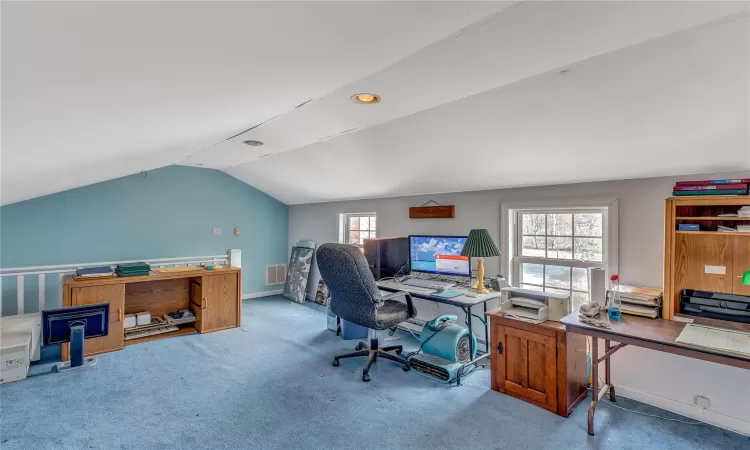 Carpeted home office with lofted ceiling, visible vents, and baseboards