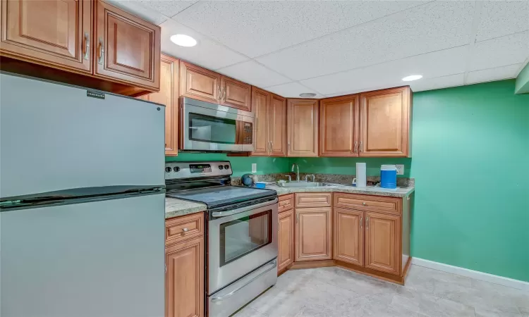 Kitchen with stainless steel appliances, a drop ceiling, a sink, and baseboards