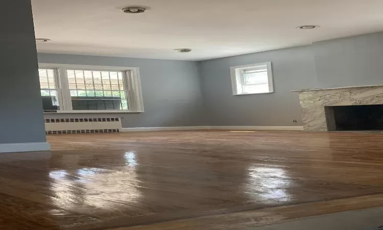 Unfurnished living room featuring a premium fireplace, baseboards, radiator, and wood finished floors