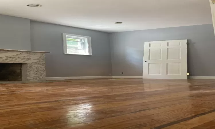 Unfurnished living room with wood finished floors, baseboards, and a high end fireplace