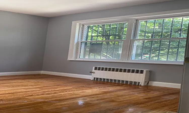 Unfurnished room with baseboards, wood finished floors, and radiator heating unit