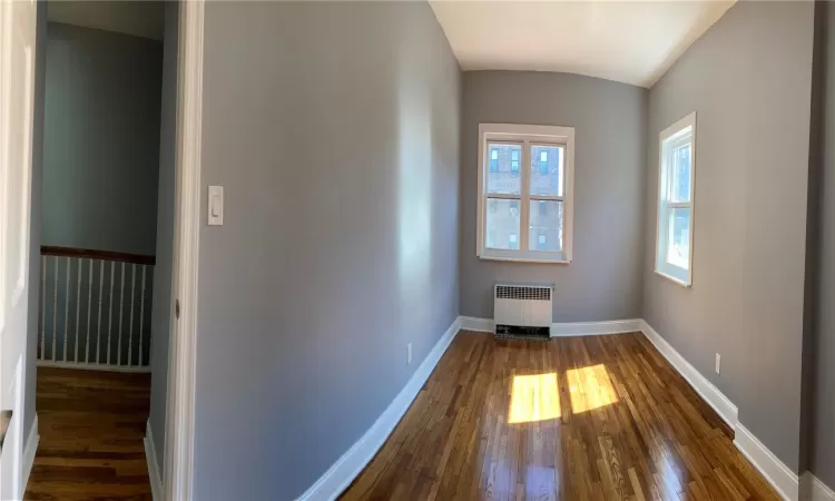 Spare room with a healthy amount of sunlight, radiator, dark wood-type flooring, and baseboards