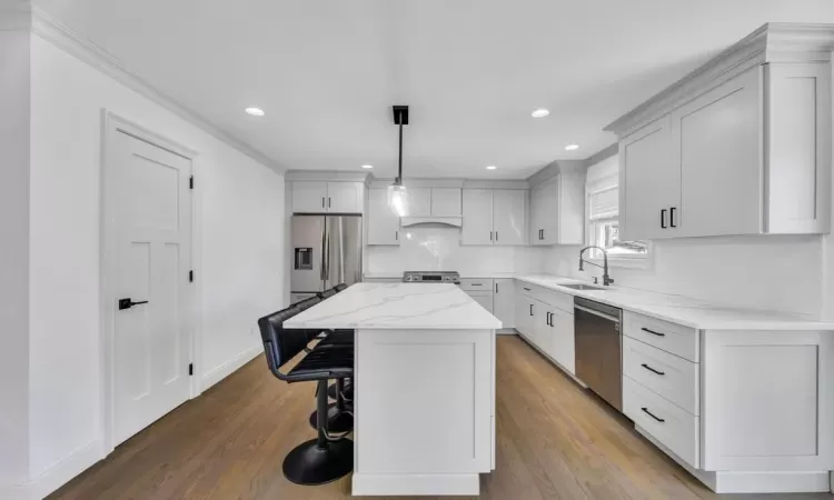 Kitchen featuring a breakfast bar area, a kitchen island, dark wood-style flooring, a sink, and appliances with stainless steel finishes