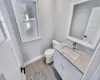 Bathroom featuring vanity, wood finished floors, baseboards, visible vents, and toilet