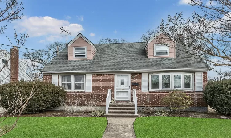 Cape cod home featuring a front yard, brick siding, and roof with shingles